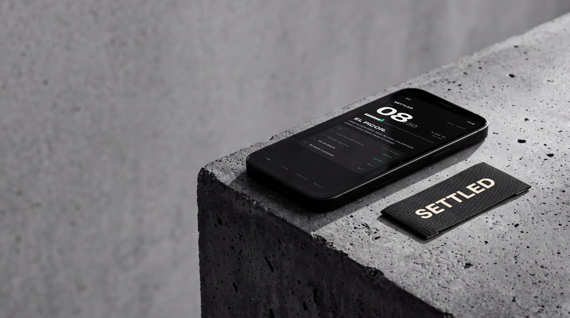 Phone showing the Settled screen on a concrete block next to a black woven label