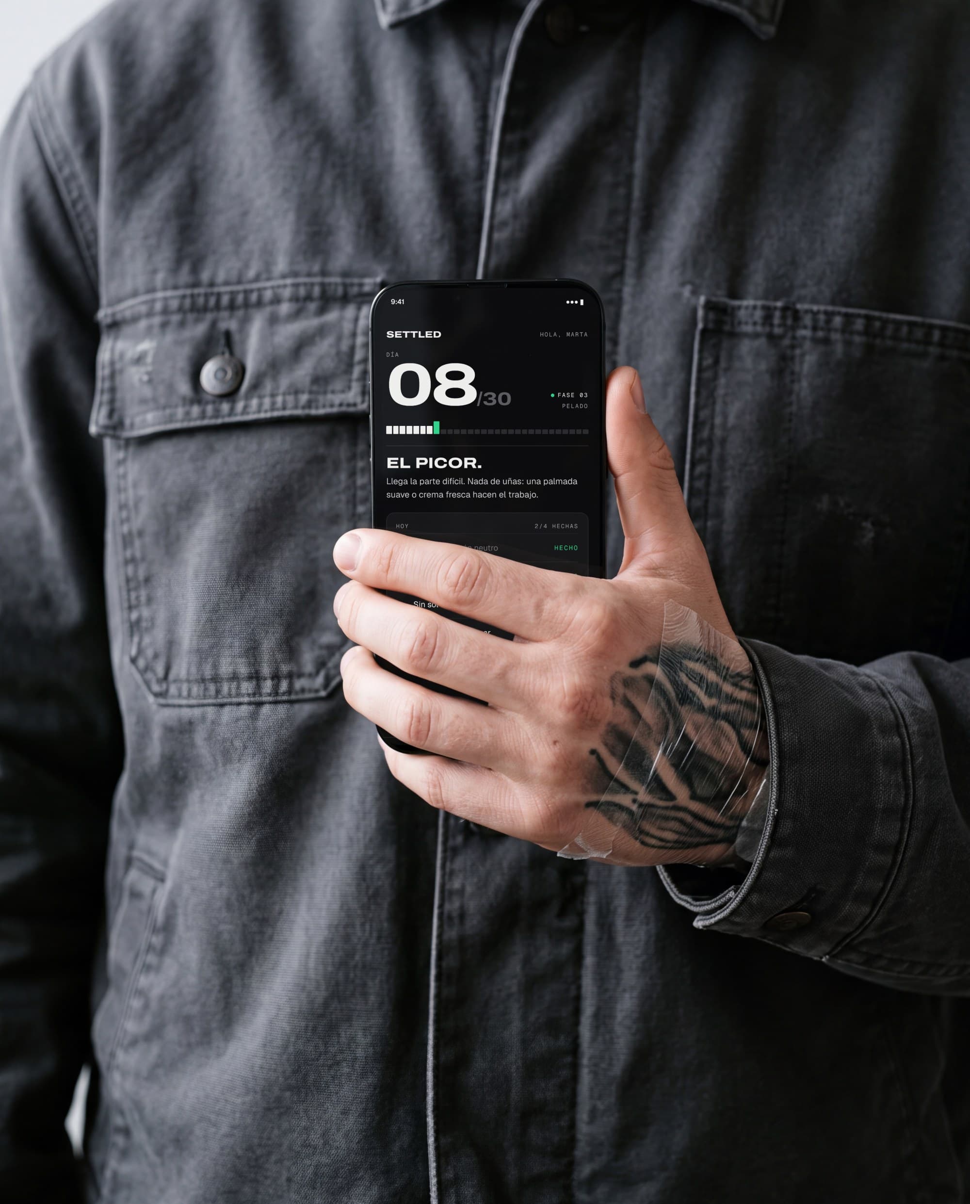 Hand with a tattoo under film holding a phone showing the Settled screen